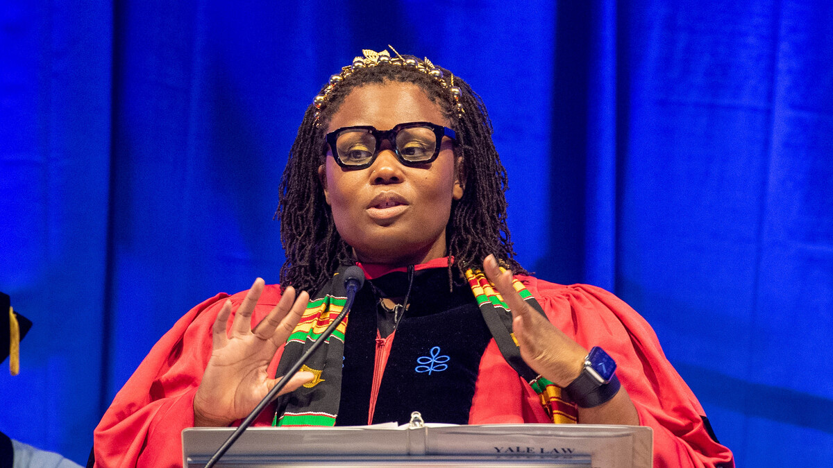 Monica Bell speaking at the podium at commencement wearing a red academic gown