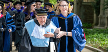 Two figures processing in regalia arm in arm